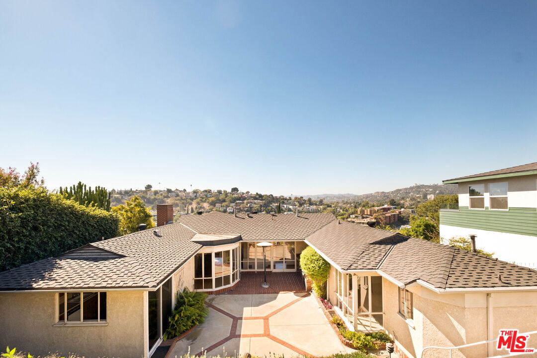 Single-story home surrounding a paved courtyard, with hillside homes visible beyond.