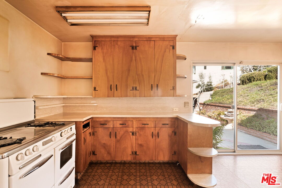 Kitchen with wood cabinetry, a white gas range, and sliding glass doors to a garden.
