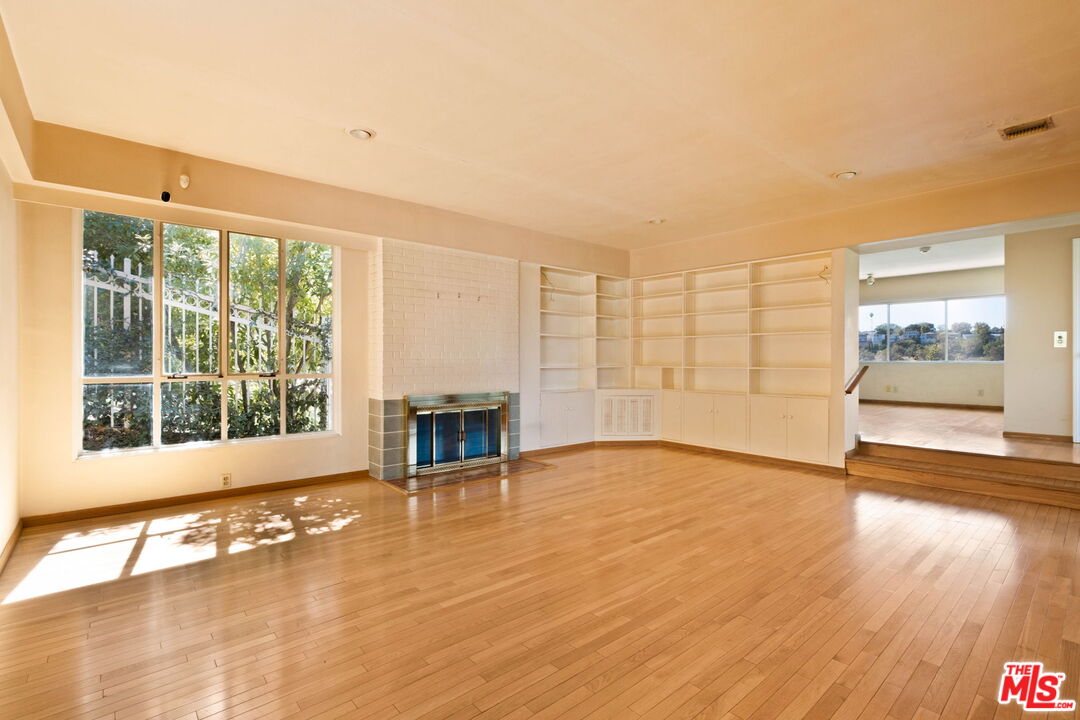 Vacant living room with hardwood floors, a fireplace, and built-in shelving beside a large window.