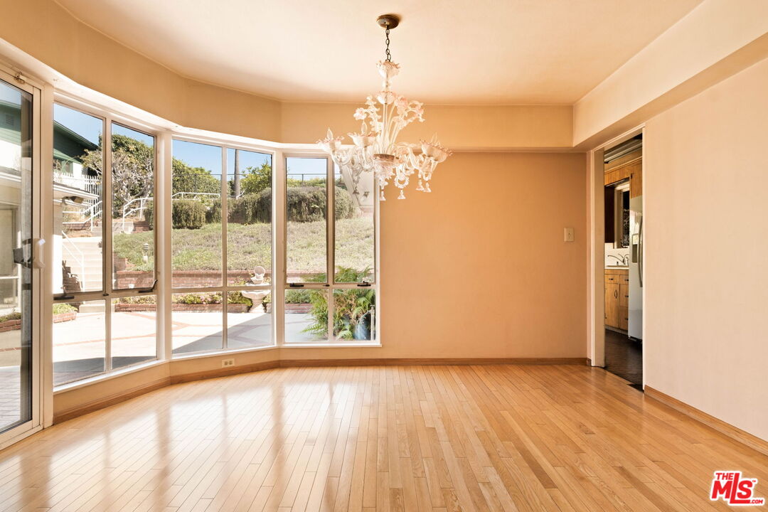Empty dining room with curved floor-to-ceiling windows, polished hardwood floors, and a white chandelier.