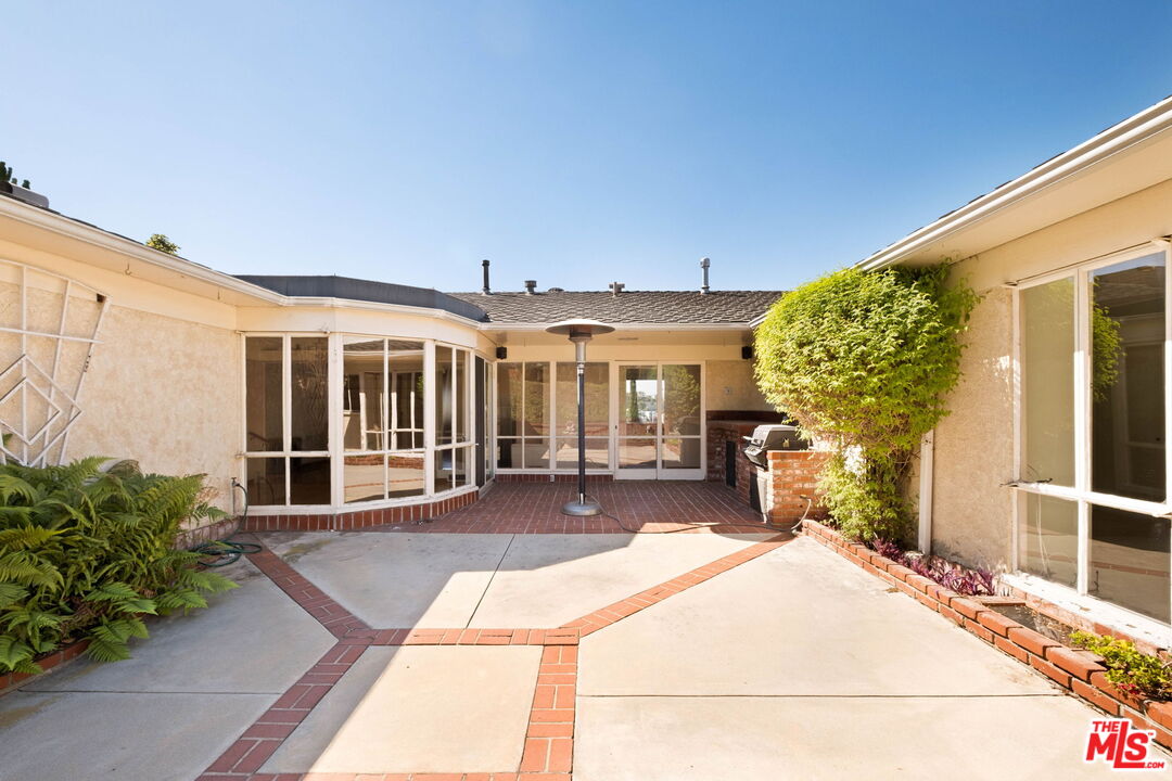 Enclosed courtyard patio with brick-edged paving, glass doors, and a grill.