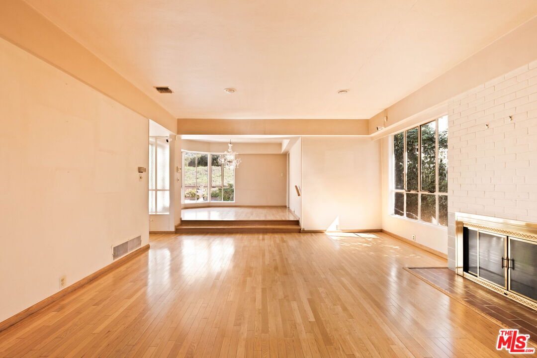 Vacant living room with hardwood floors, a white brick fireplace, and a raised area at the back.