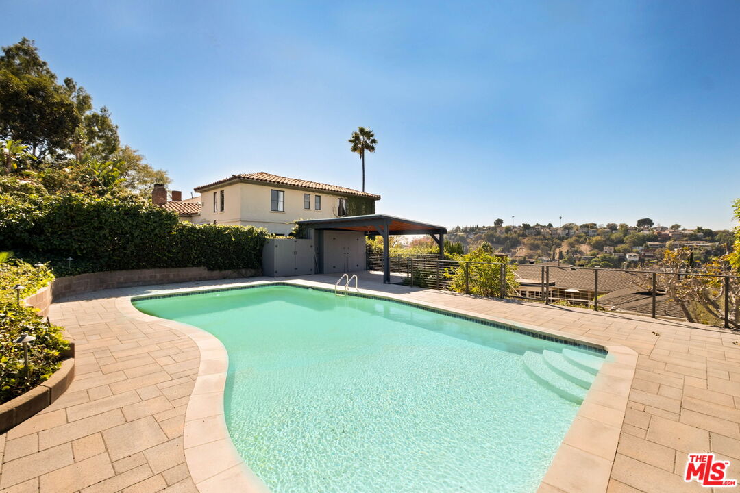 Backyard swimming pool and paved patio overlooking hillside homes.