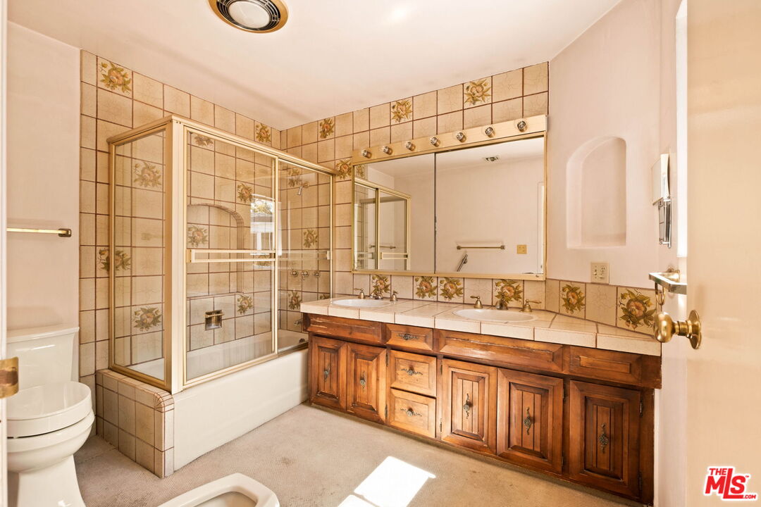 Bathroom with floral tile, glass-enclosed tub and shower, and long wood vanity.