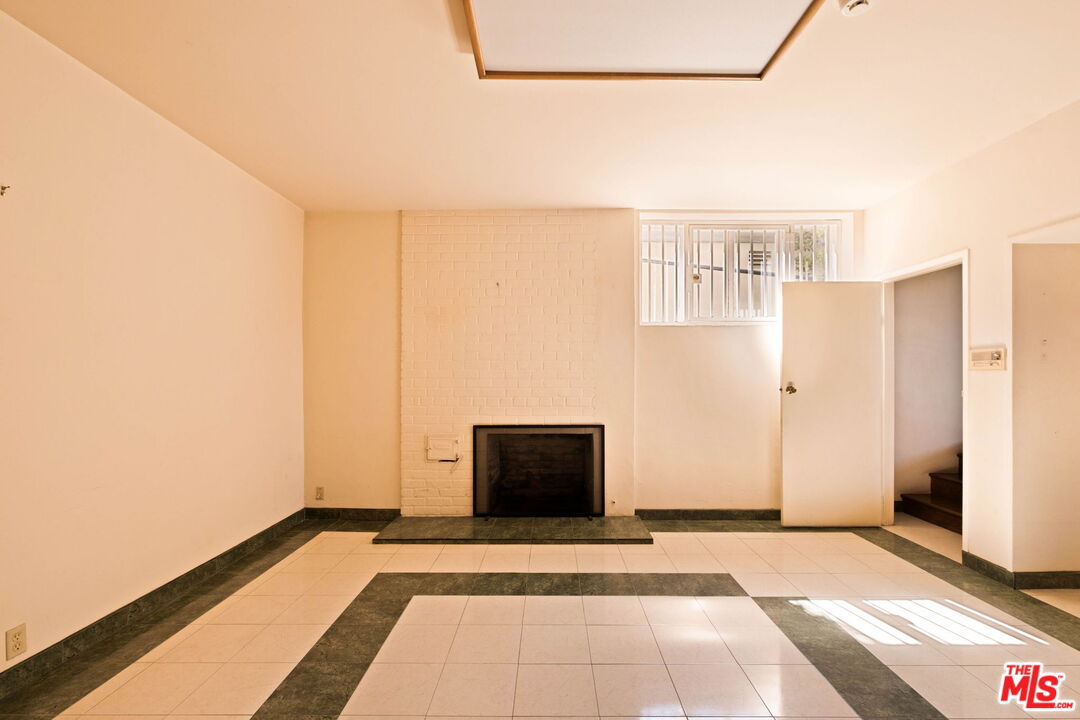Vacant living room with a white brick fireplace, geometric tile floor, and stairs through an open doorway.