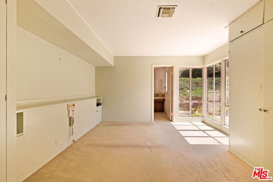 Unfurnished carpeted room with built-in cabinetry and sunny glass doors opening toward a patio.