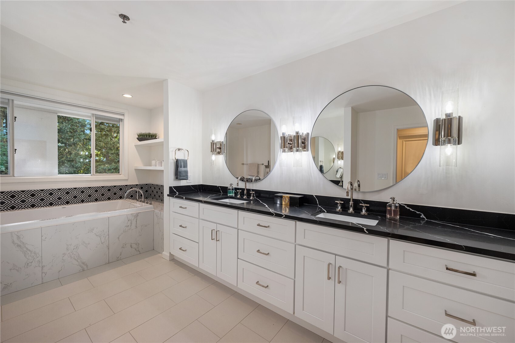 Bathroom with a double vanity and round mirrors beside a soaking tub with geometric tile.
