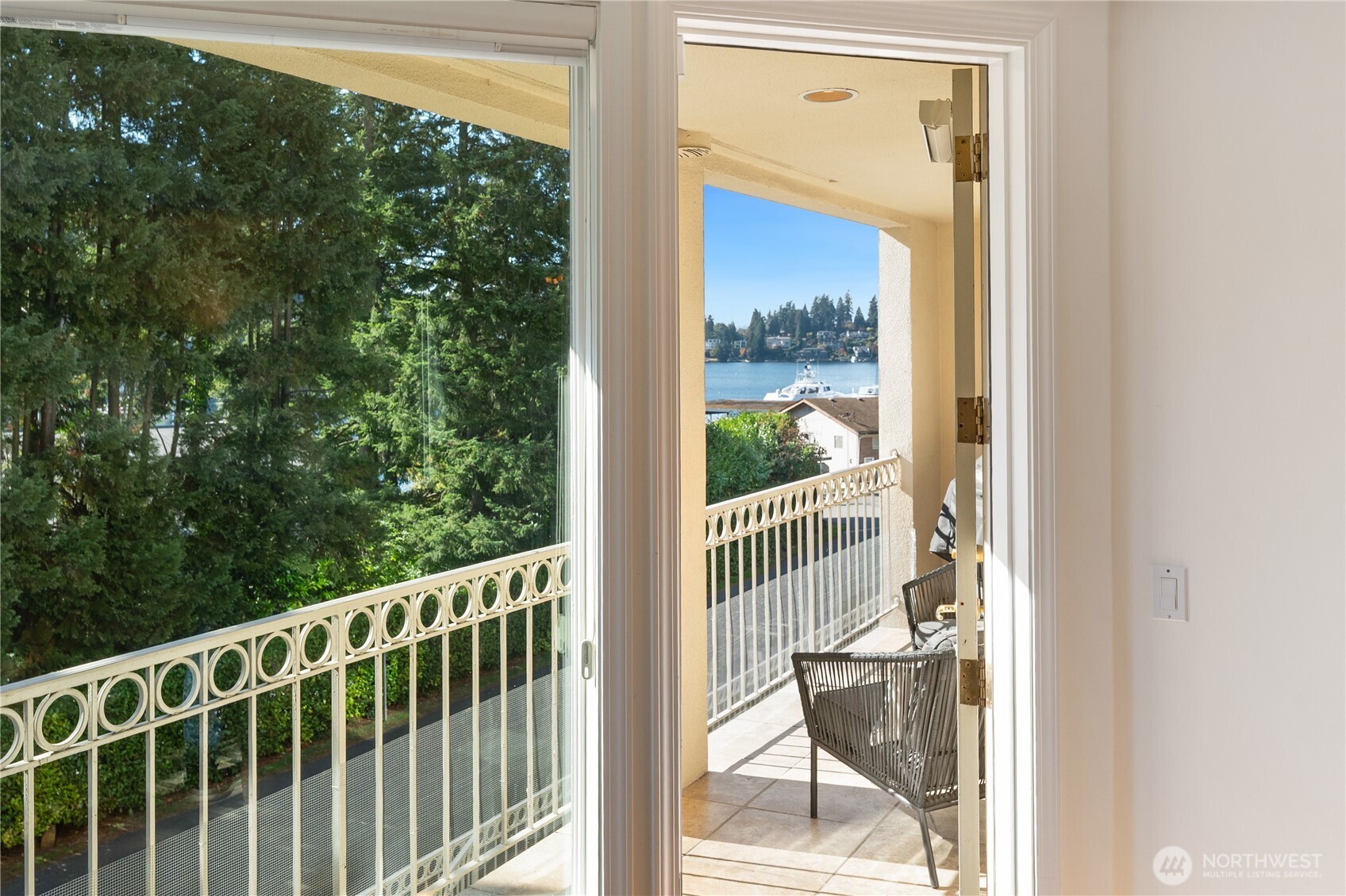 Sliding doors open to a furnished balcony overlooking the water and tree-lined shore.