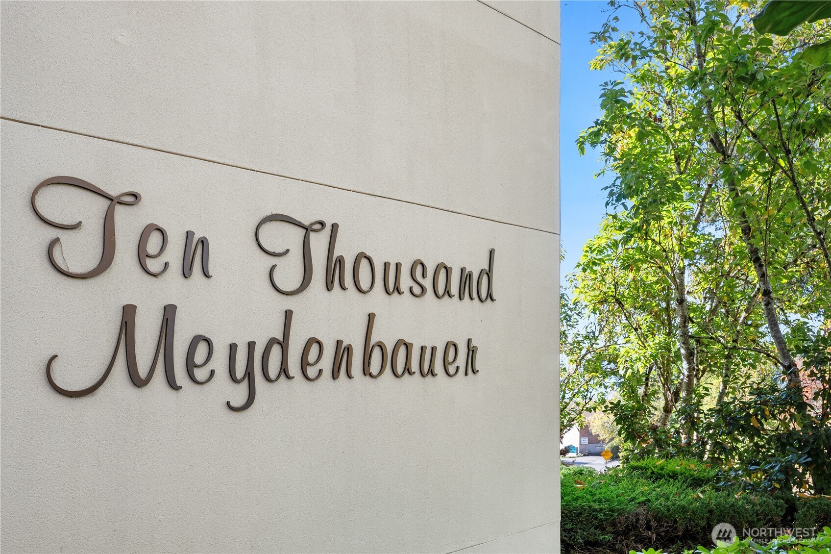 Ten Thousand Meydenbauer entrance sign on a stone wall beside leafy trees.