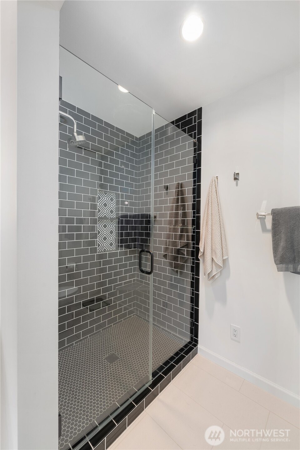Bathroom shower with dark gray subway tile, a geometric accent, and small hexagonal floor tile.