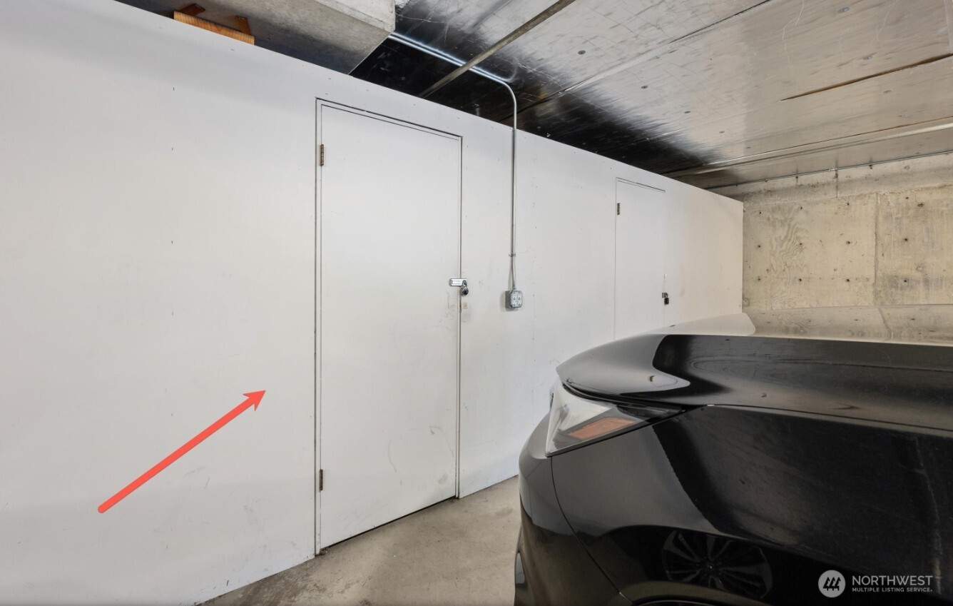 Parking garage with white storage doors, exposed concrete ceiling, and a black car; red arrow points toward the wall.