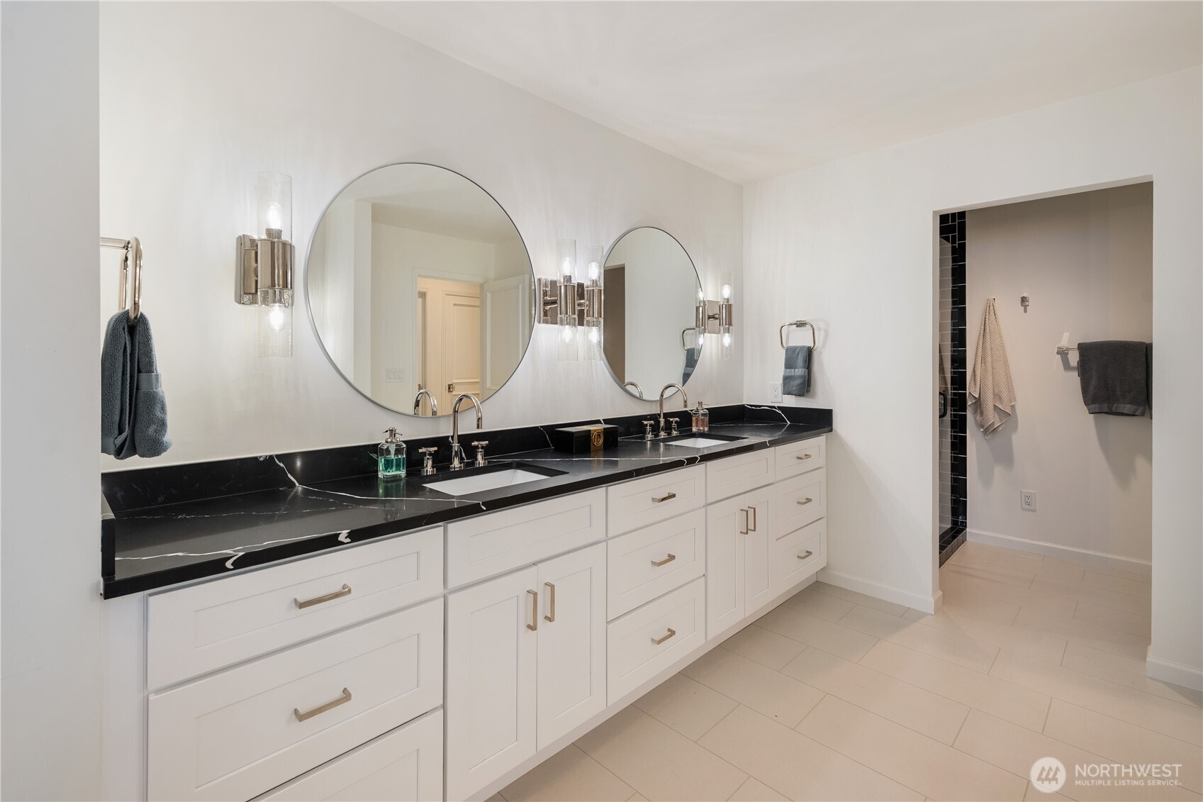 Bathroom with a double white vanity, black veined countertop, and two round mirrors.