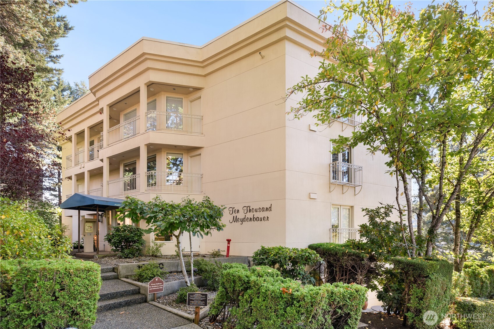 Ten Thousand Meydenbauer condominium exterior with balconies, a blue entrance canopy, and landscaped grounds.