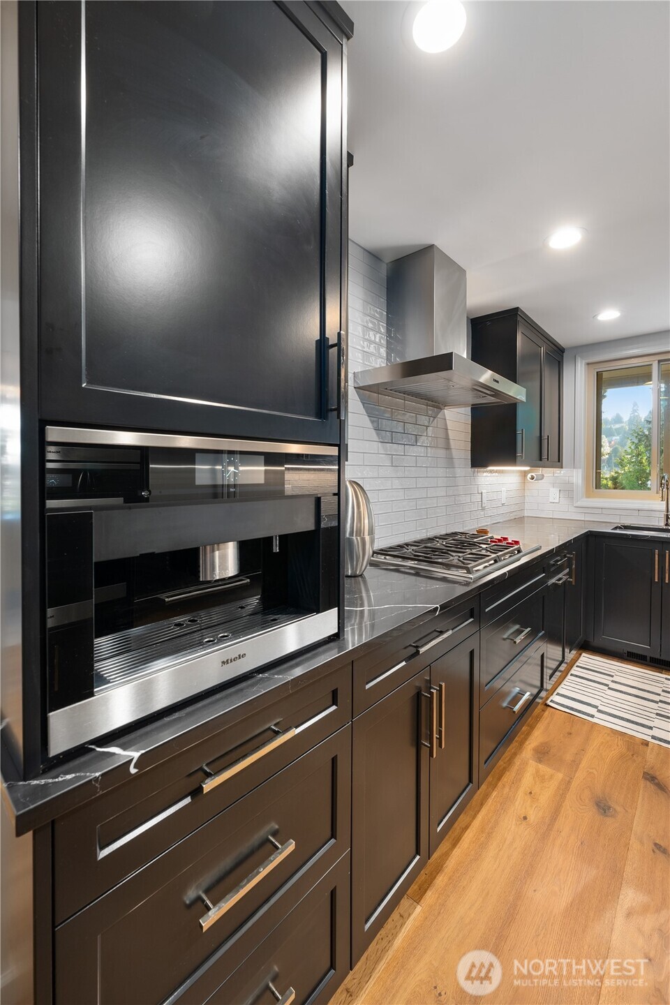 Modern kitchen with dark cabinetry, built-in Miele coffee machine, gas cooktop, and white subway tile backsplash.