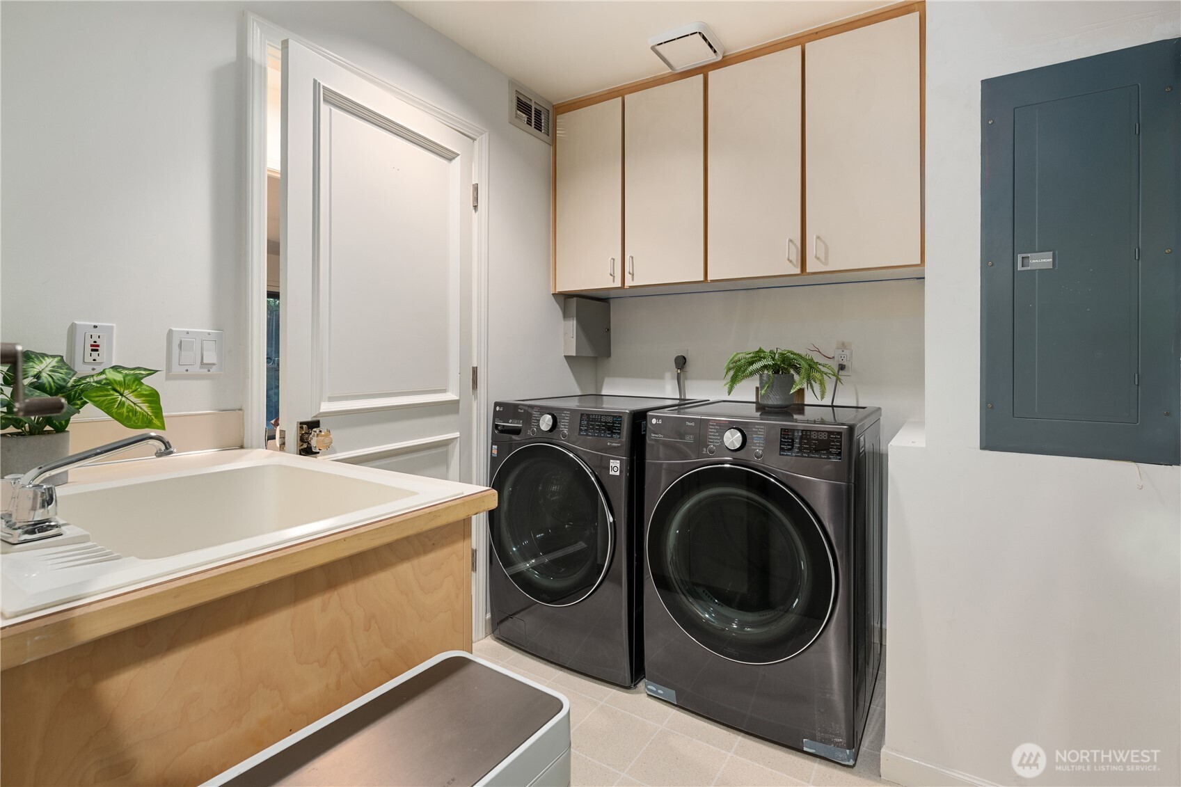 Laundry room with front-loading washer and dryer, overhead cabinets, and a utility sink.