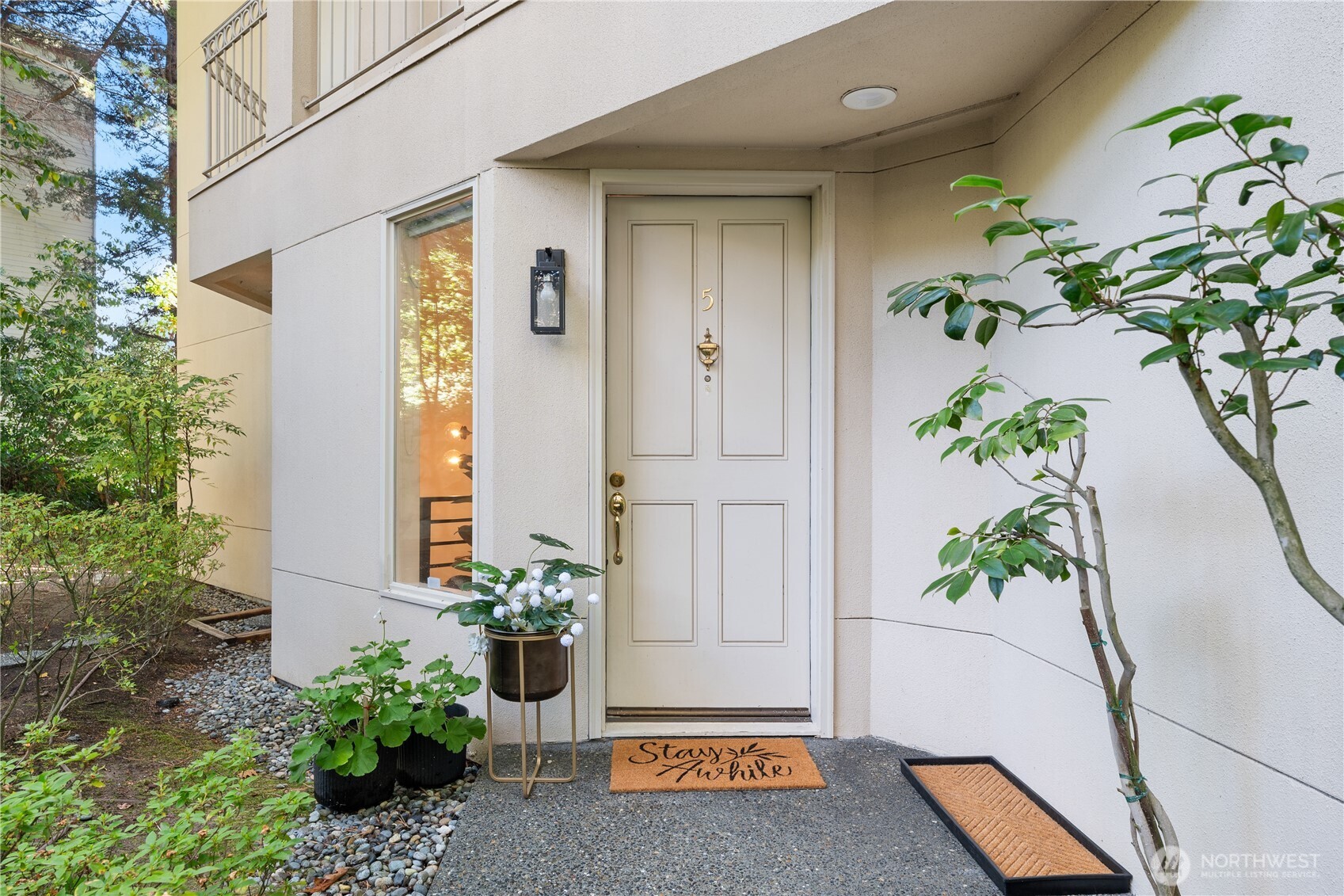 Unit 5 entrance with a white paneled door, potted flowers, and landscaped garden beds.