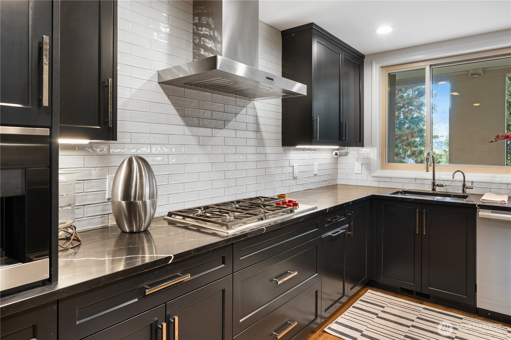 Modern kitchen with dark cabinets, a gas cooktop, and a sink beneath a large window.