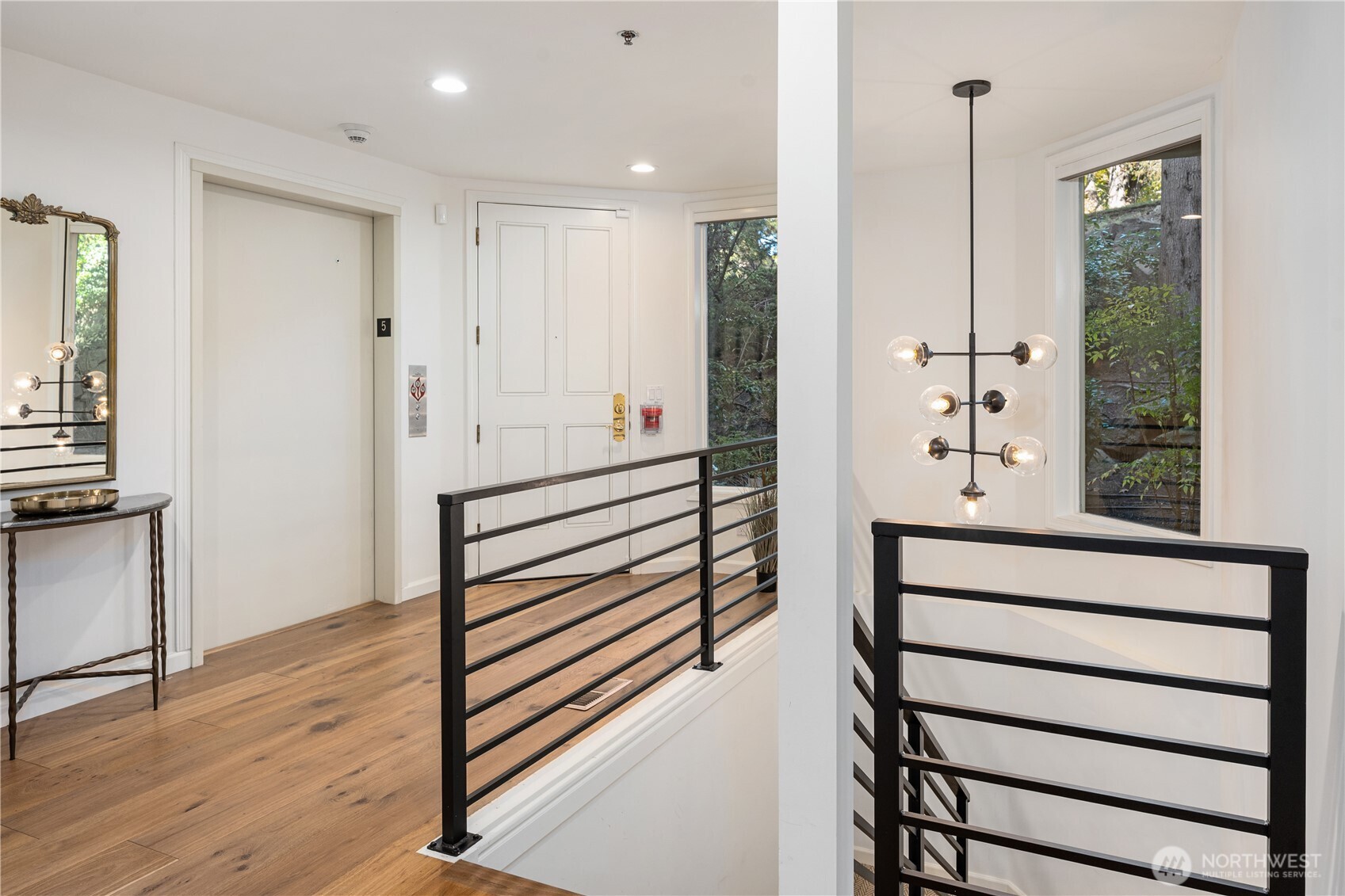 Entry landing with wood floors, black stair railings, a white door marked 5, and a globe-bulb pendant light.