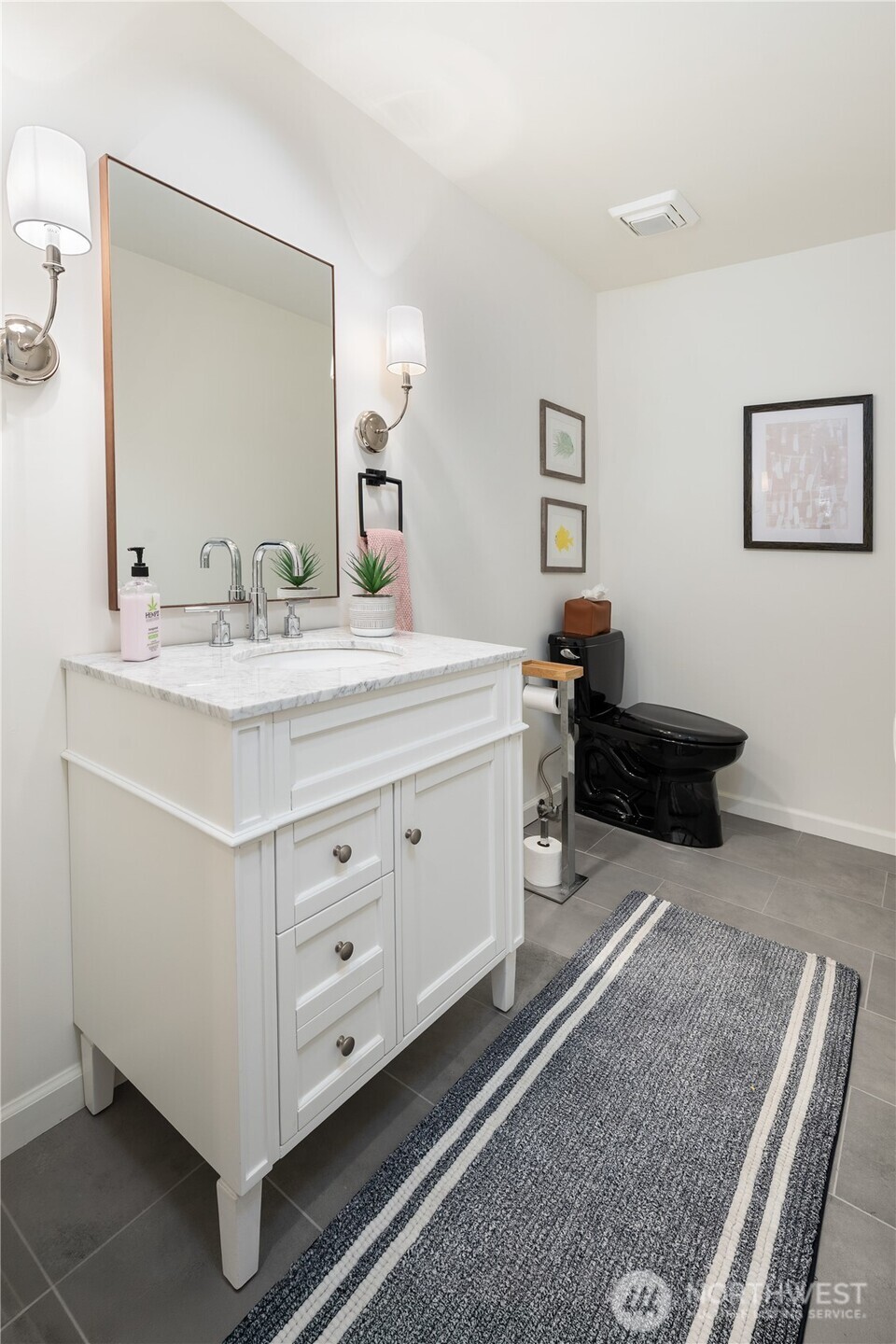 Bathroom with a white marble-top vanity, large mirror, black toilet, and striped gray rug.