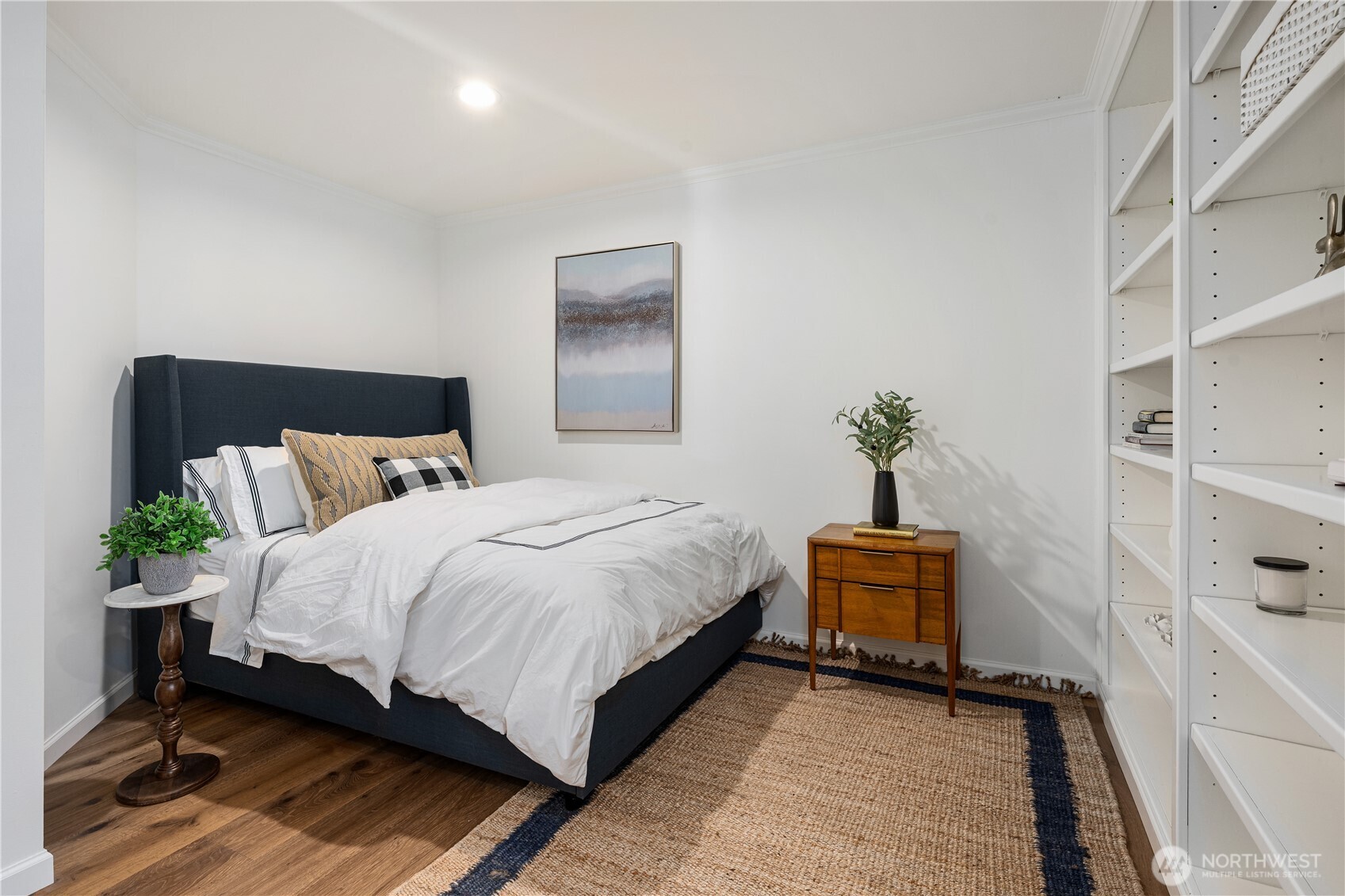 Staged bedroom with a dark upholstered bed and built-in white shelving along one wall.