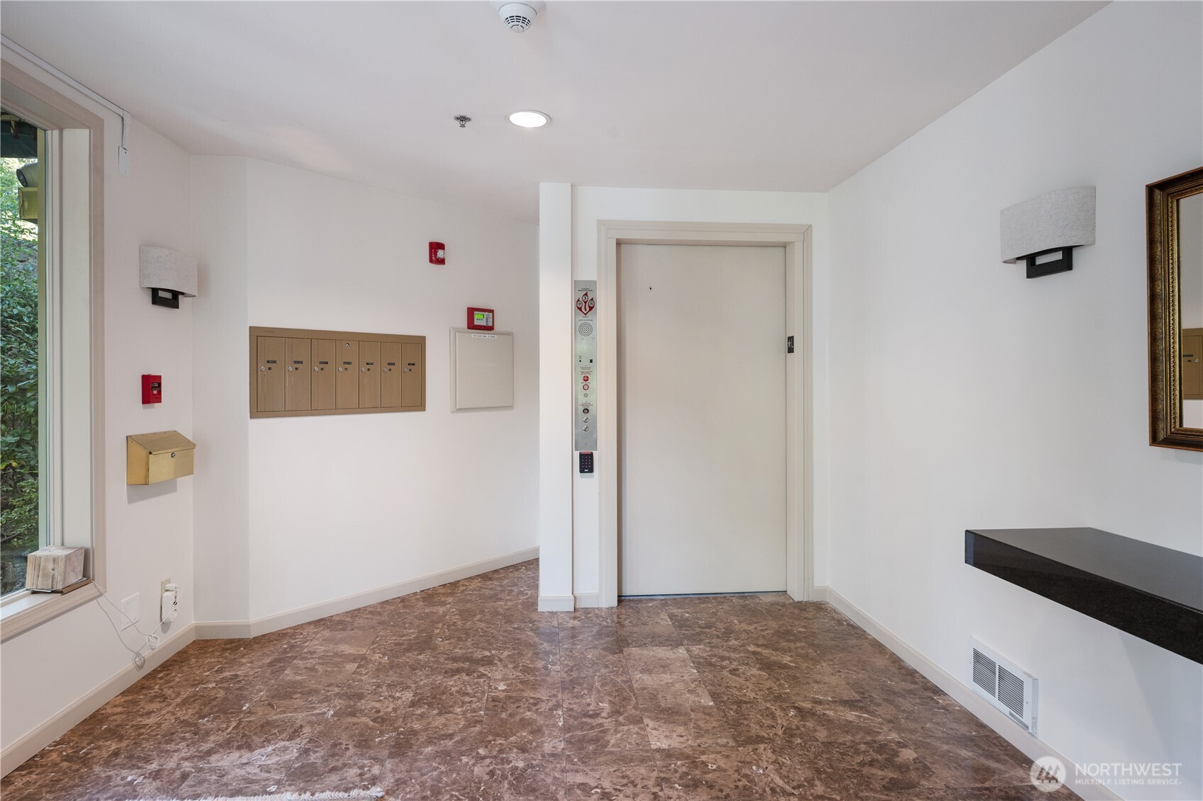 Condominium lobby with an elevator, mailboxes, and polished brown stone tile flooring.