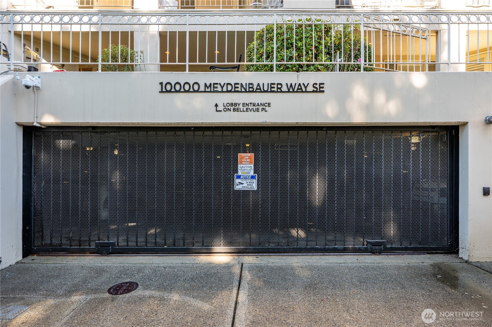 Condominium entrance with the 10000 Meydenbauer Way SE address sign above a closed mesh garage gate.