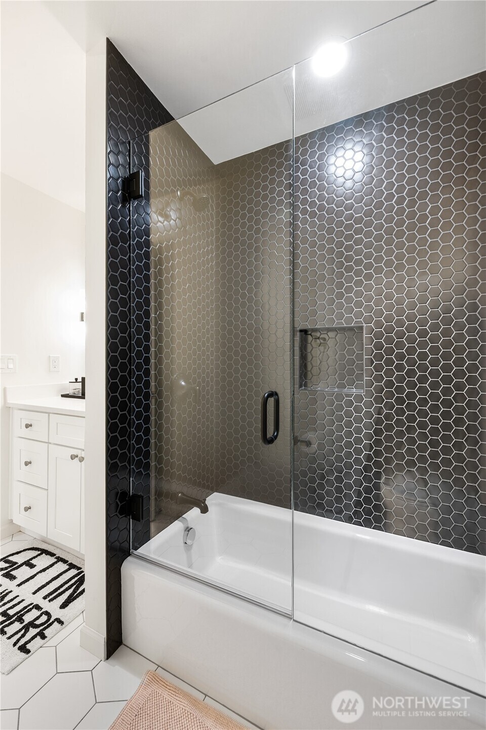 Bathroom tub and glass shower with dark hexagonal tile and a built-in wall niche.