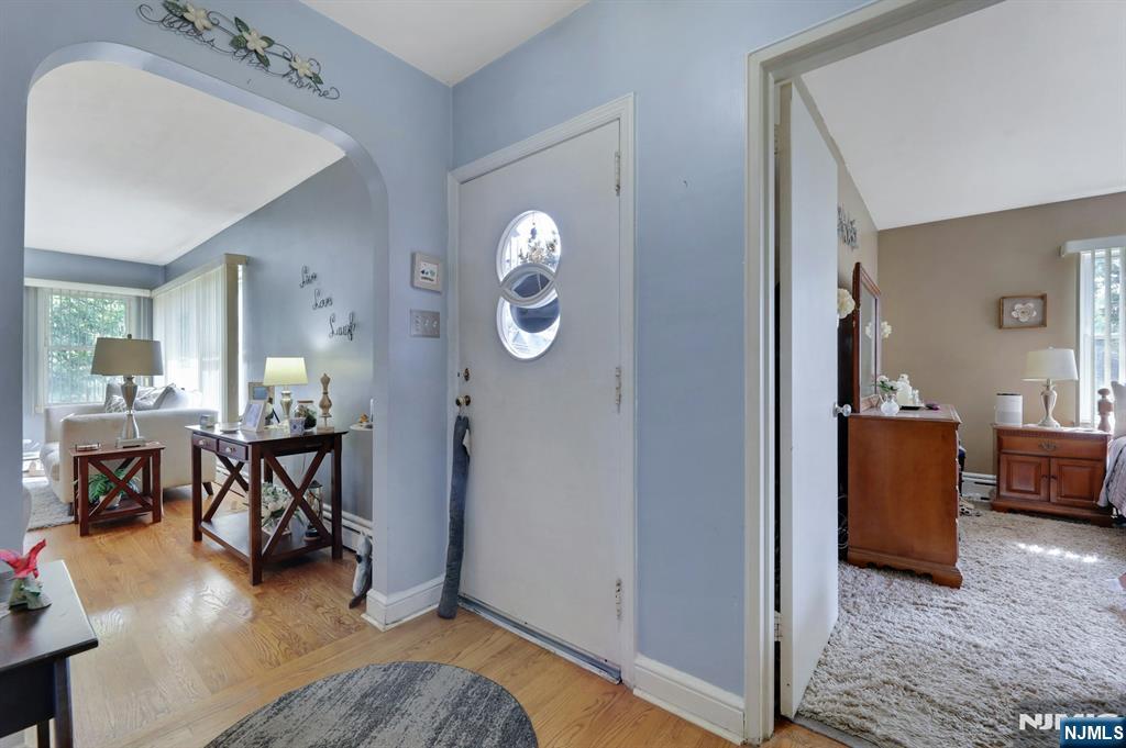 Entry foyer with oval-windowed front door, hardwood flooring, and openings to furnished rooms.