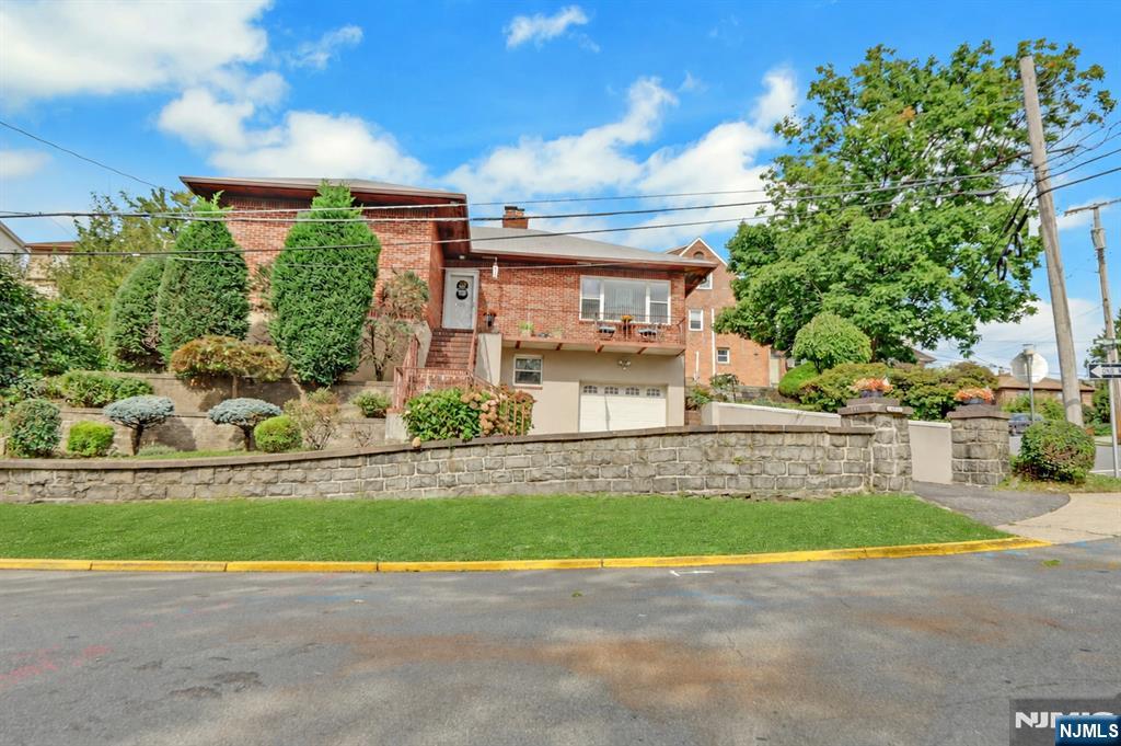 Raised brick house with a balcony and garage behind a stone retaining wall.