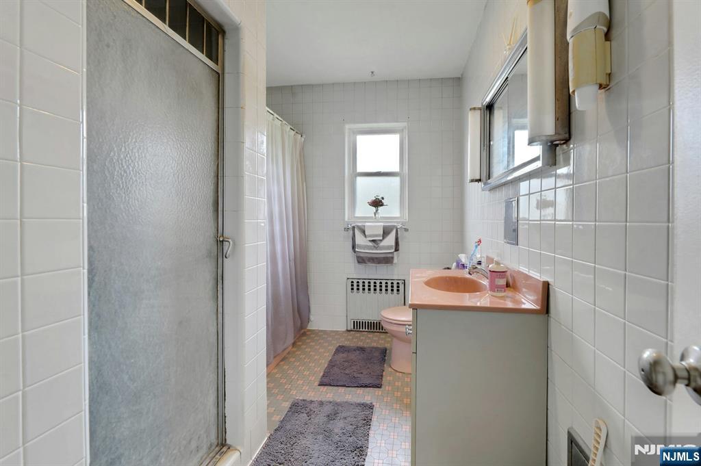 Tiled bathroom with a frosted-glass shower, pink sink countertop, and small window.