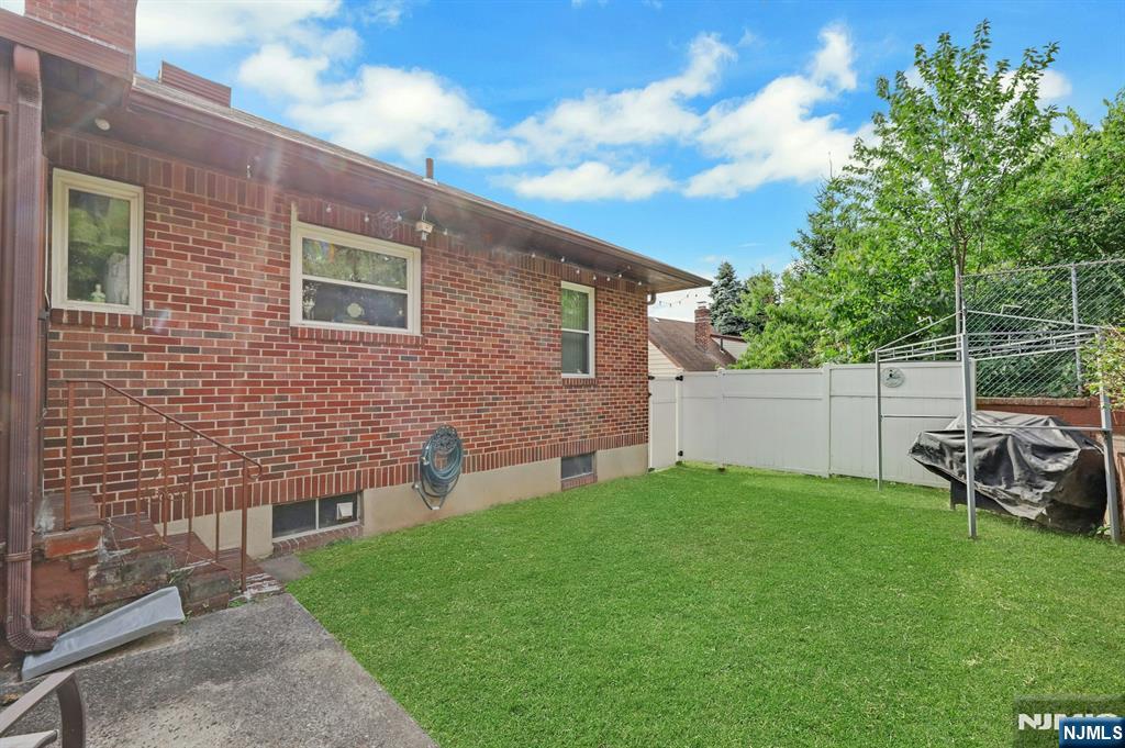 Brick house backyard with a fenced lawn, concrete patio, and covered grill.