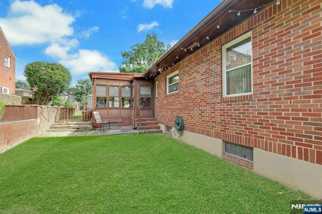 Backyard with a green lawn, brick exterior, and enclosed porch.