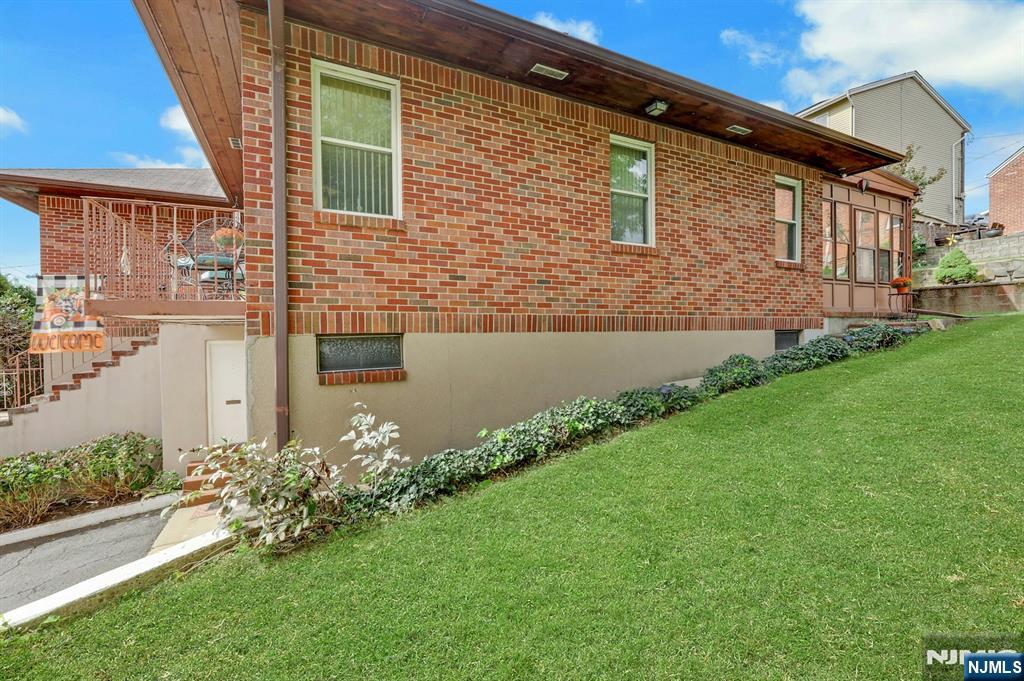 Brick house with a covered patio, basement-level window, and sloping lawn.