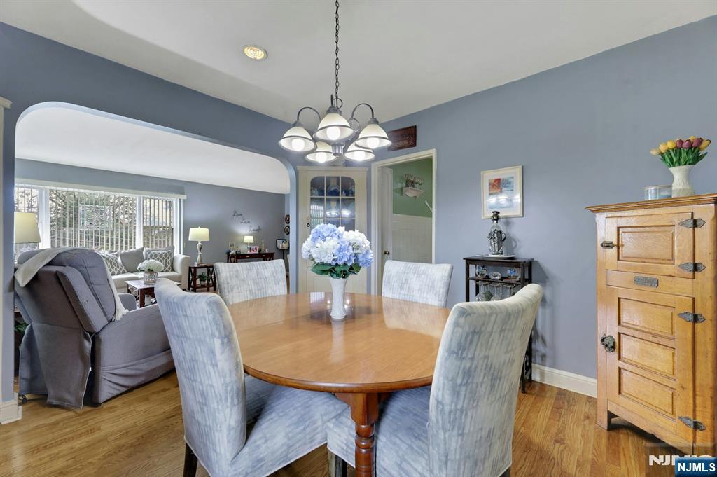 Dining room with an oval wood table, upholstered chairs, chandelier, and adjoining living area.