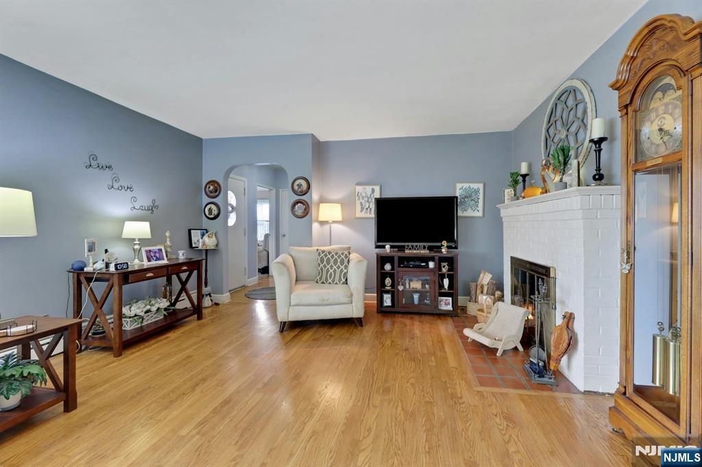 Living room with hardwood floors, blue-gray walls, a white brick fireplace, and a tall wooden grandfather clock.
