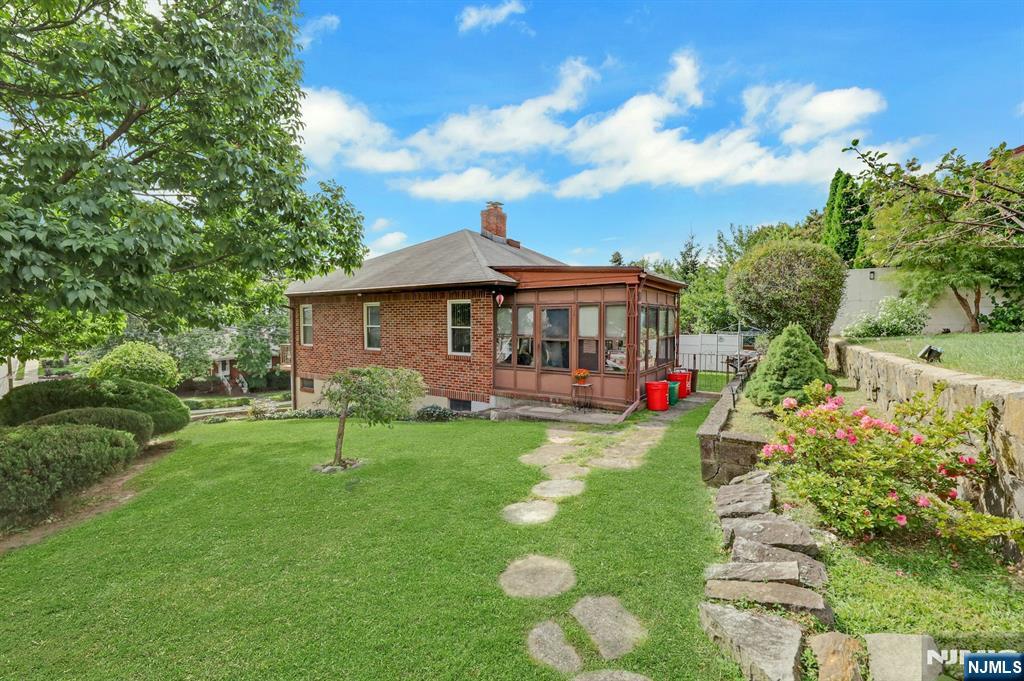 Brick house with an enclosed sunroom and landscaped backyard bordered by a stone retaining wall.