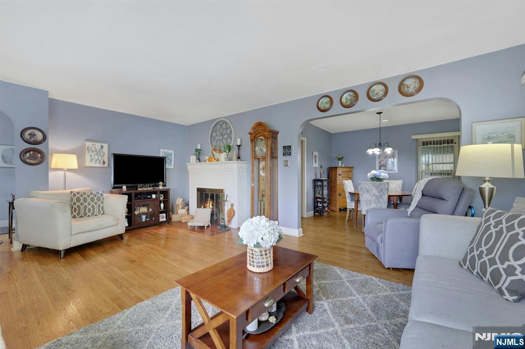 Living room with a white fireplace, hardwood floors, and an arched opening to the dining area.