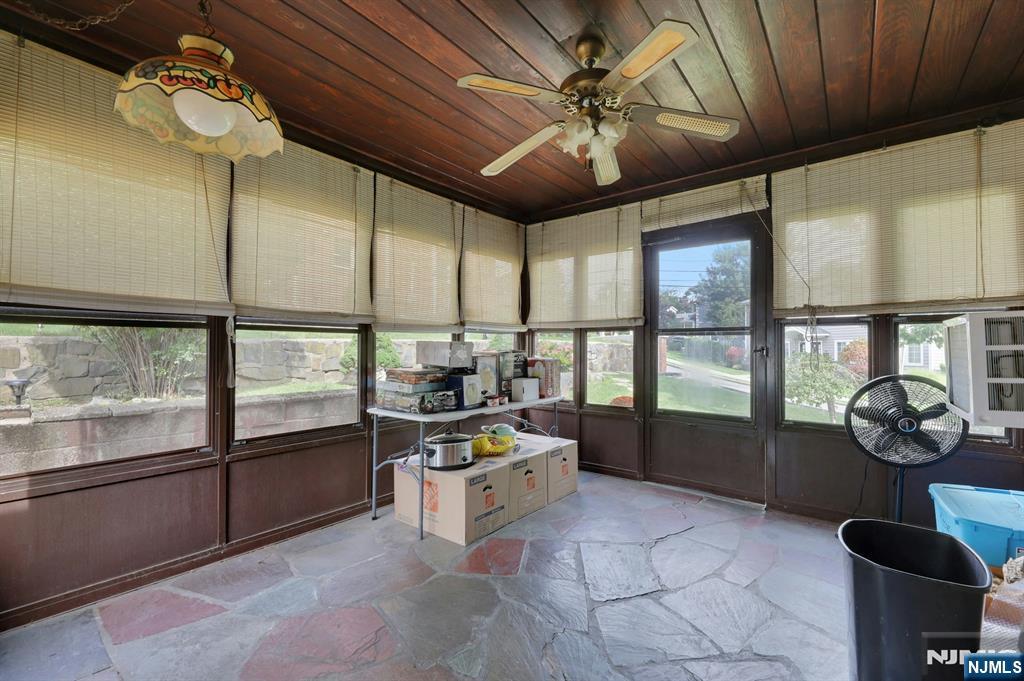 Enclosed sunroom with a wood-paneled ceiling, stone tile floor, and windows overlooking the yard.