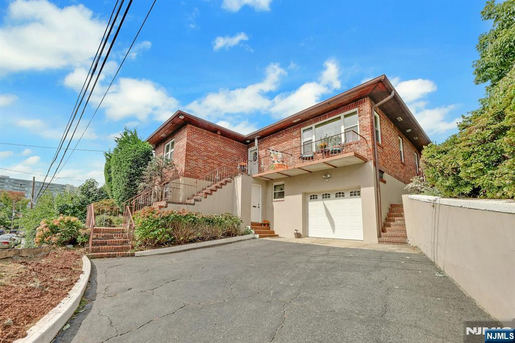 Two-story brick home with elevated entry, balcony, attached garage, and broad driveway.