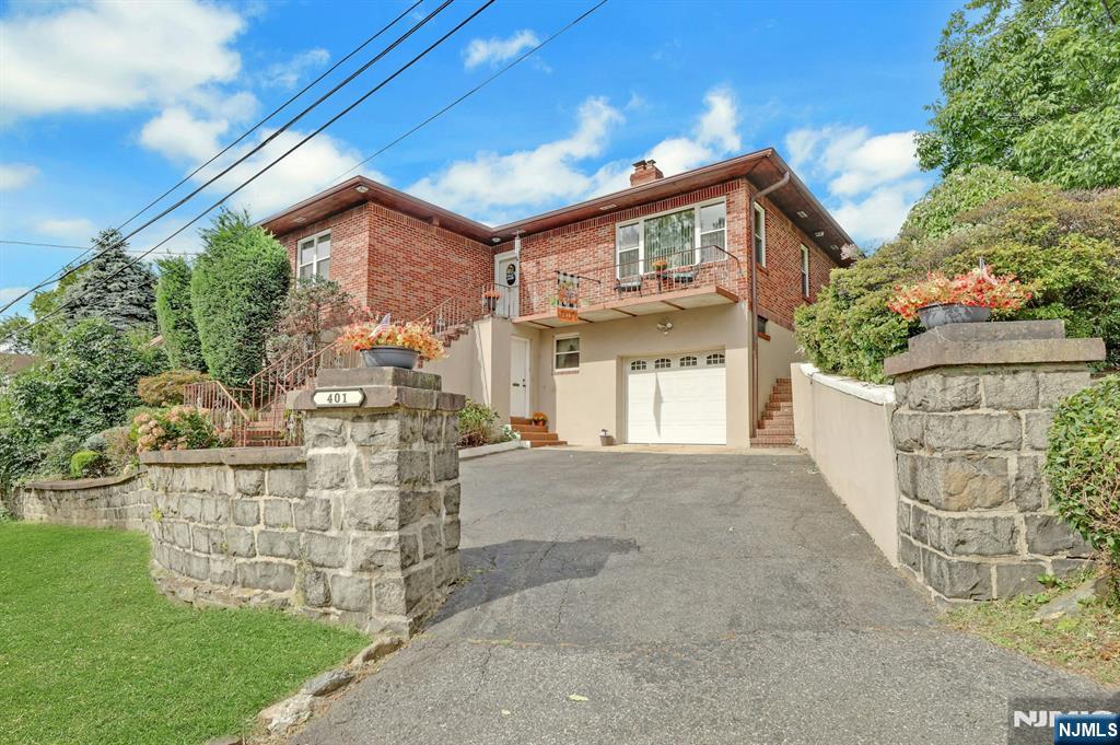 Red-brick house with a white garage and balcony, approached by a driveway between stone walls.