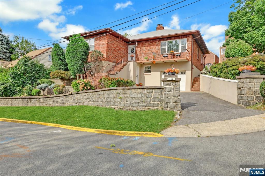 Brick home with exterior stairs, a small balcony, stone wall, and landscaped front yard.