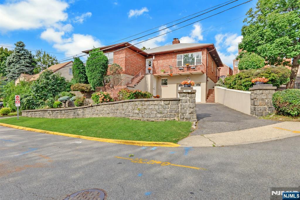 Brick two-story house with a balcony, exterior stairs, stone retaining wall, and sloped driveway.