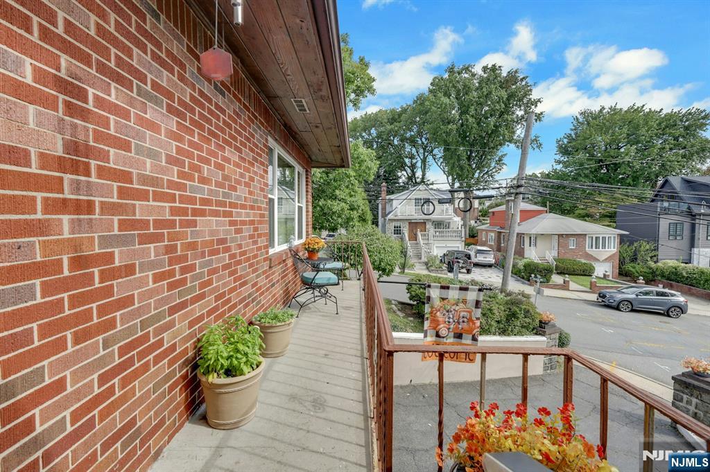 Brick home’s raised porch with potted plants and chairs overlooking a residential street.