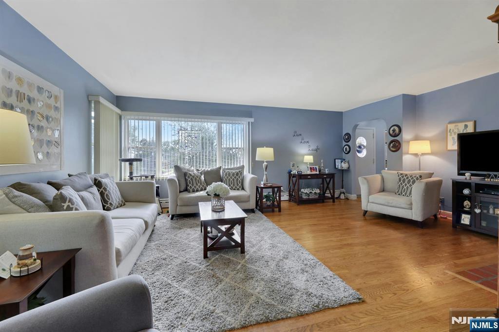 Furnished living room with cream sofas, hardwood floors, and a large window with vertical blinds.
