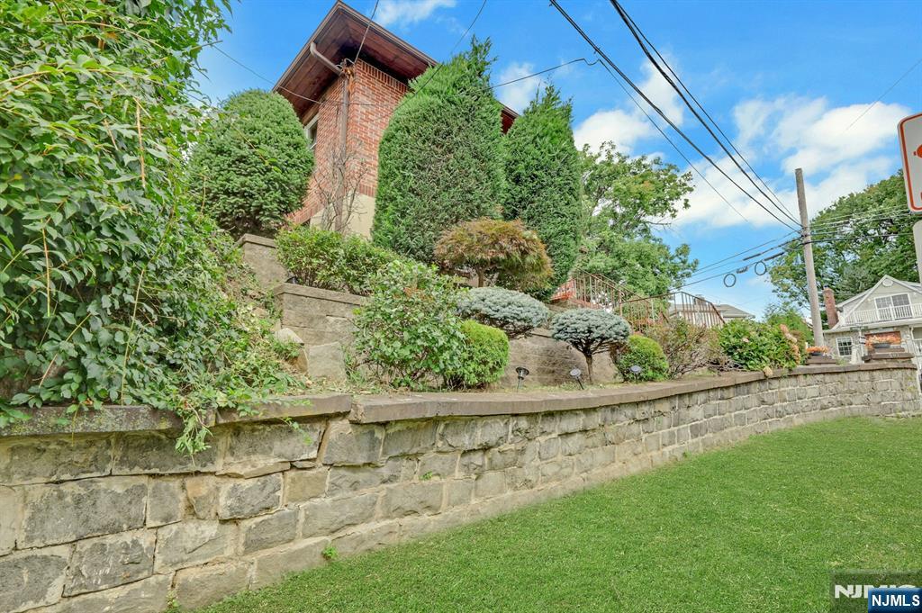Brick house behind mature landscaping and a stone retaining wall beside a lawn.