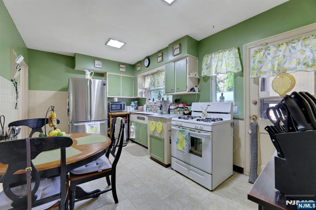 Kitchen with green cabinets, a stainless steel refrigerator, and a dining table beside the gas range.