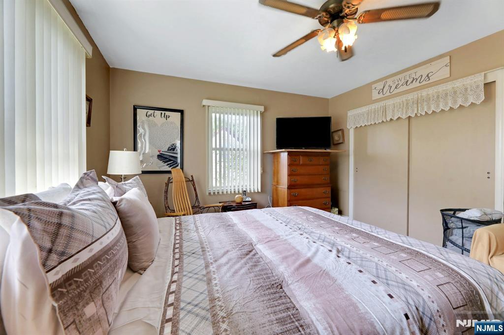 Bedroom with a patterned bed, ceiling fan, and television on a wooden dresser.