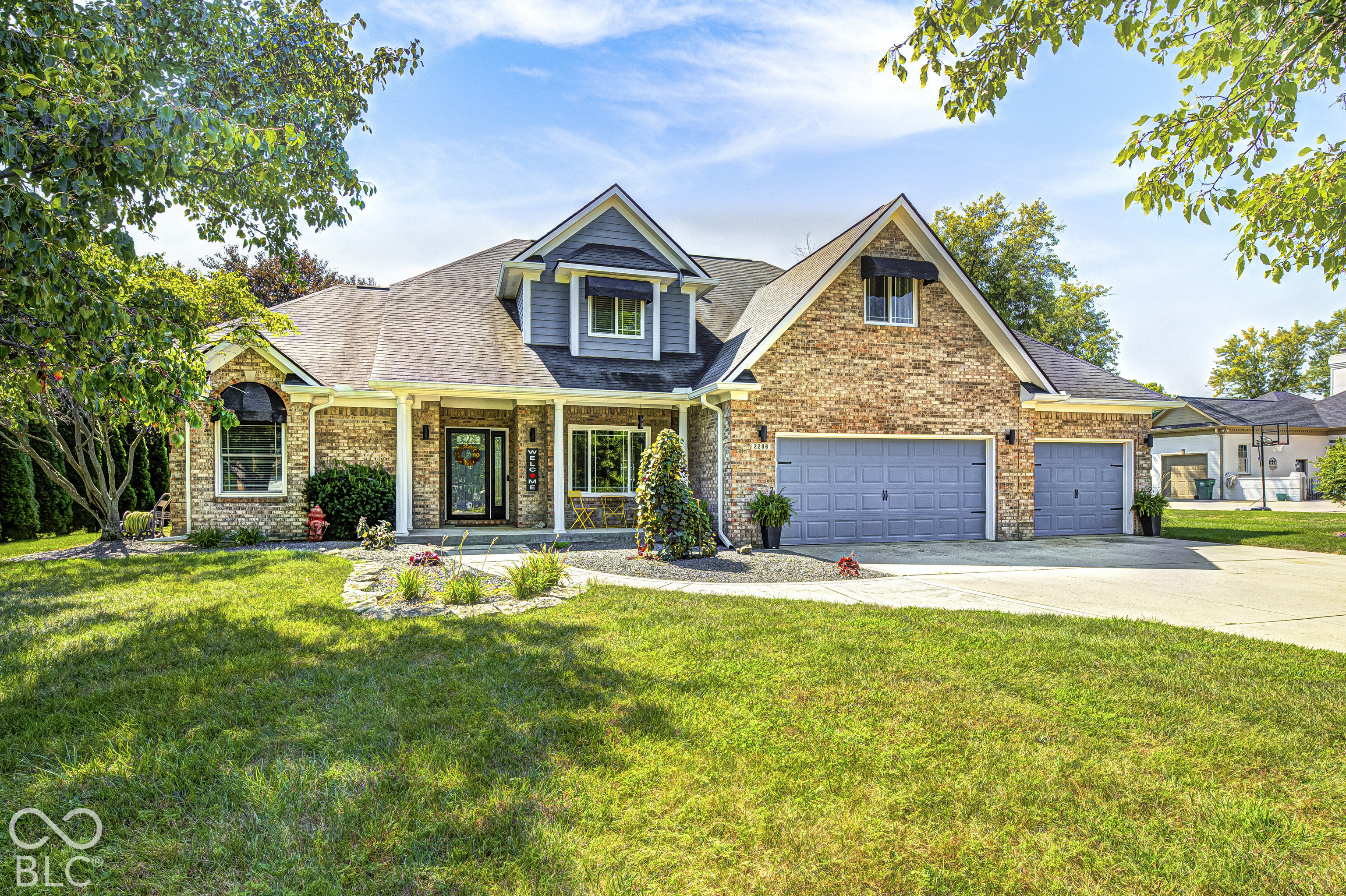 Two-story brick house with gray gables, a covered porch, double garage, and landscaped front lawn.