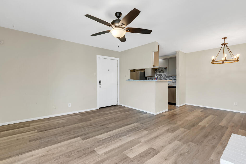 Unfurnished living and dining area with wood-look floors, ceiling fan, and open kitchen.