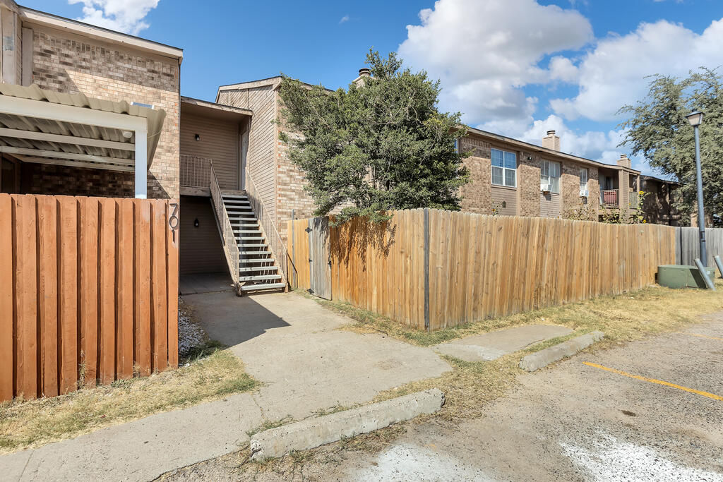 Brick apartment building behind a wooden privacy fence, with exterior stairs and a parking area.